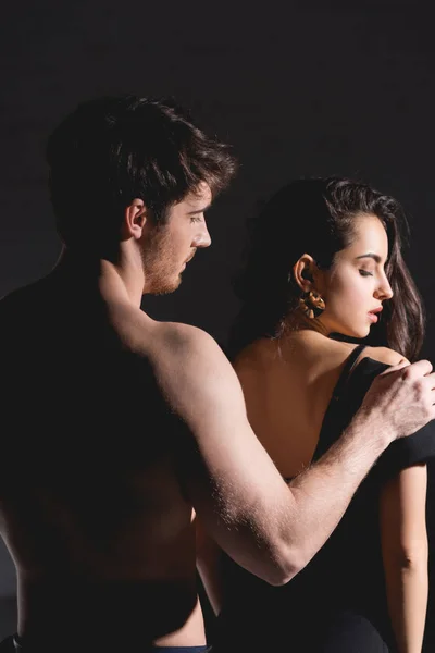 shirtless man standing back and undressing woman on black background