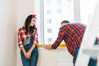 cheerful woman looking at boyfriend measuring heating radiator clipart