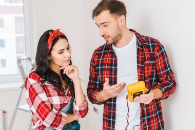 handsome man holding digital multimeter while standing near woman at home clipart