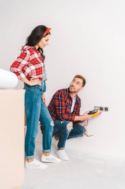 yakışıklı adam elektrik prizine oturan ve evde kadına seyir sırasında dijital multimetre holding