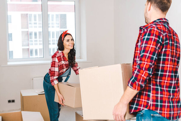 happy woman holding box and looking at man at home