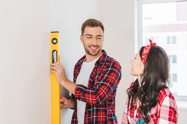 Cheerful Man Holding Measuring Level Girlfriend Home — Stock Photo, Image