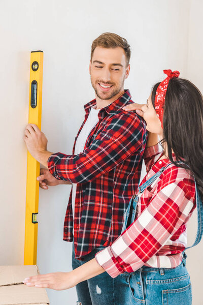 happy man holding measuring level near girlfriend at home