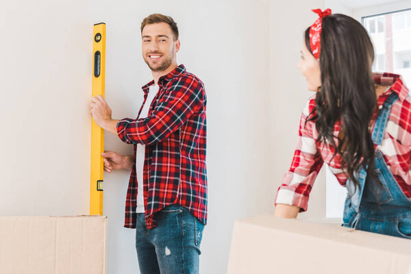 selective fcous of happy man holding measuring level near girlfriend at home