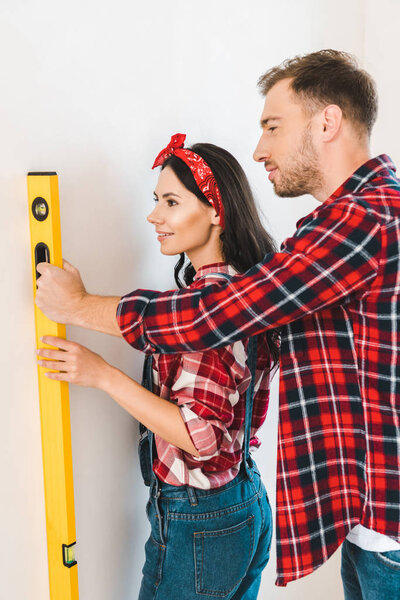 happy couple holding measuring level near wall at home