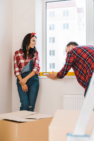 selective focus of cheerful woman looking at boyfriend measuring heating radiator