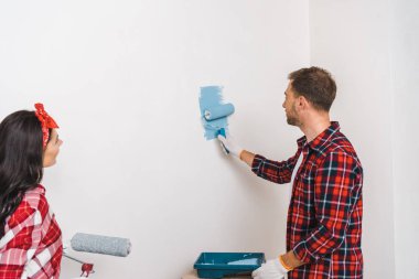  man painting wall in blue color near woman holding roller  clipart