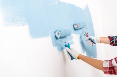 cropped view of man and woman painting wall in blue color at home clipart