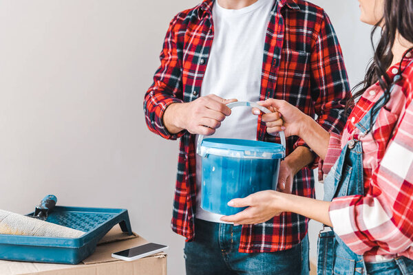cropped view of man taking paint bucket and standing near woman at home