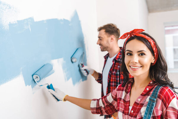 selective focus of attractive woman holding roller near man painting wall