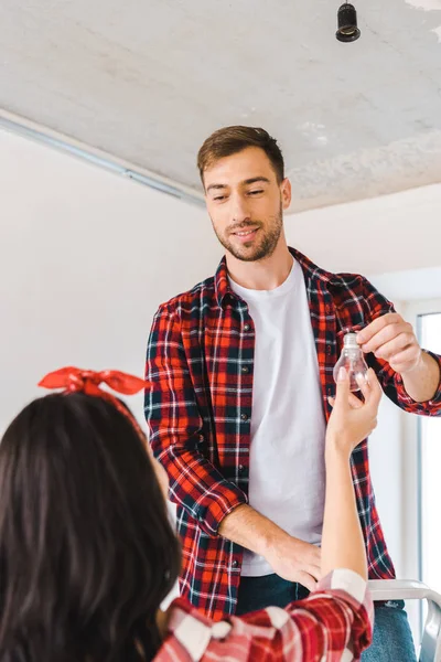 Knappe Man Staande Een Ladder Nemen Lamp Terwijl Vriendin Kijken — Stockfoto