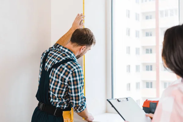 selective focus of handyman measuring window near female client