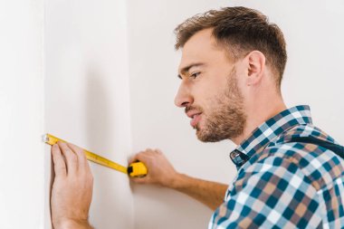 yakışıklı tamirci ayakta ve teyp duvarının yakınında ölçme holding