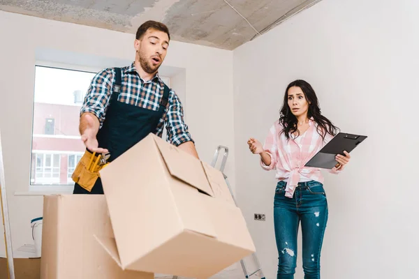 Förvånad Kvinna Som Tittar Fallande Box Nära Handyman — Stockfoto