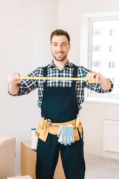 cheerful handyman smiling while holding measuring tape 