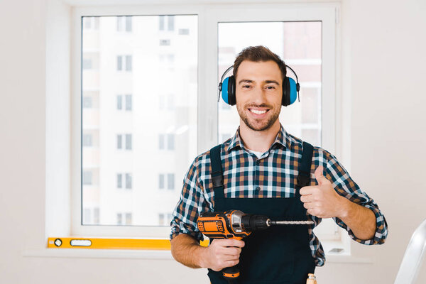 handsome handyman showing thumb up while holding drill in hand