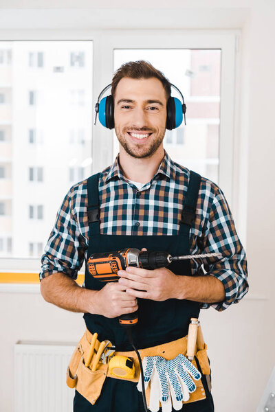 handsome handyman smiling while holding drill in hands