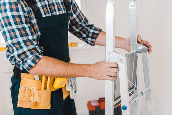 cropped view of handyman holding ladder in room