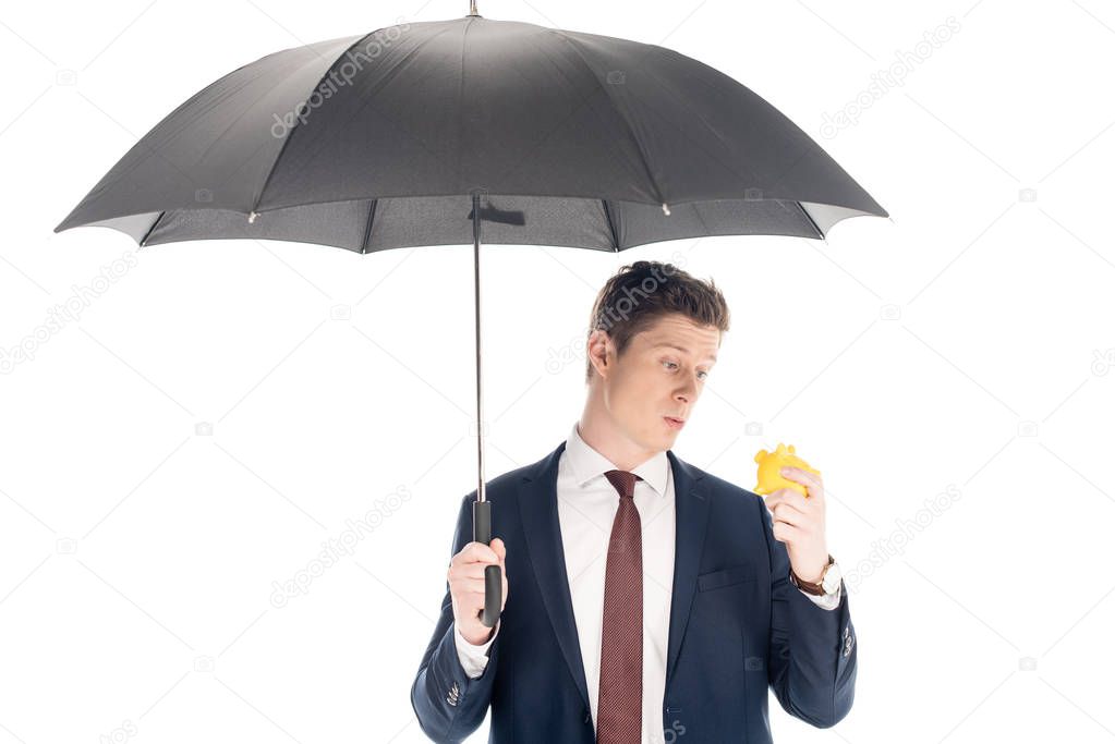 young businessman with umbrella looking at little piggy bank isolated on white 