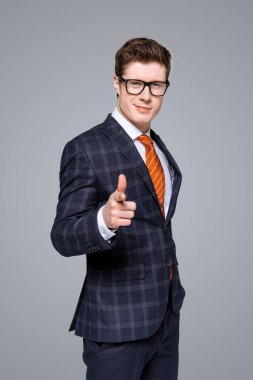 successful stylish businessman smiling and pointing at you isolated on grey