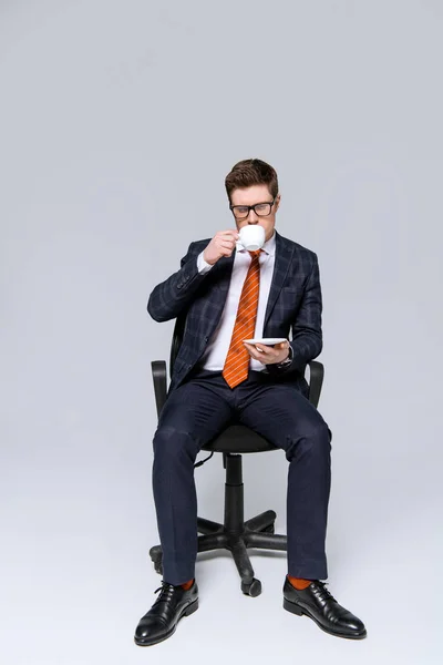 スタイリッシュなビジネスマンの椅子に座っていると灰色でコーヒーを飲む — ストック写真