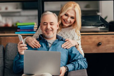 sarışın kadın kucaklama gülümseyen koca smartphone tutarken laptop arıyorum