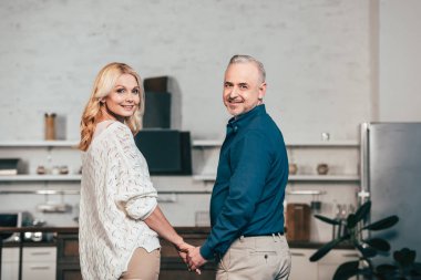 mutlu çift ayakta ve ellerini tutarak kameraya bakıyor