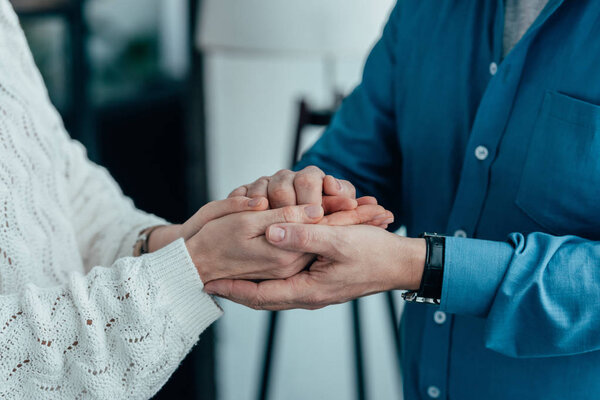 cropped view of couple holding hands at home