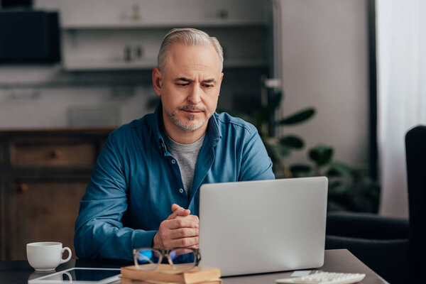 selective focus of exhausted man looking at laptop at home