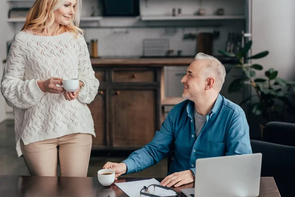 Lycklig Man Sitter Nära Laptop Och Tittar Fru Håller Cup — Stockfoto