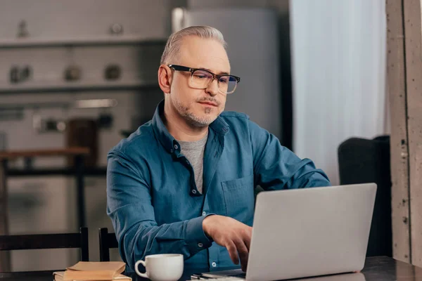 Homem Bonito Óculos Usando Laptop Perto Copo Com Bebida — Fotografia de Stock