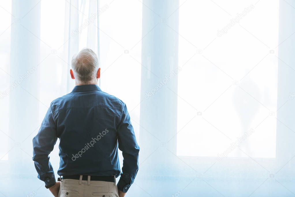 back view of man standing near window at home