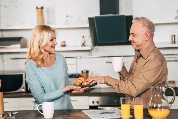 Alegre Esposa Celebración Plato Con Croissants Cerca Marido Con Taza —  Fotos de Stock