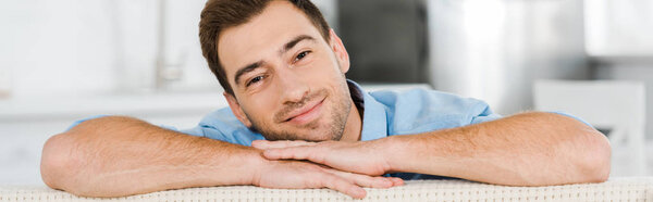 handsome smiling man looking at camera while leaning face on hands at home 