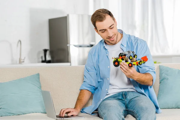 英俊的男人坐在沙发上 拿着玩具车在家里 — 图库照片