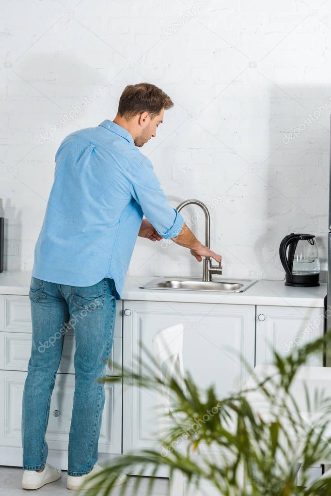 back view of man in casual clothes washing hands in kitchen