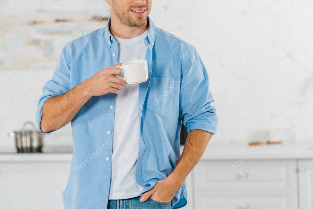 cropped view of smiling man in casual clothes drinking coffee in kitchen