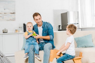 okul öncesi çocuk sürme ahşap sallanan at oturan ve evde kanepede yürümeye başlayan çocuk oğlu ile oynarken babası ise