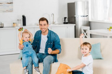 mutlu baba ise vakit ve preschooler ve yürümeye başlayan çocuk oğulları dairede tezahürat ile oynarken kameraya bakıyor