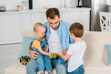 evde oyuncak arabalar ile oynarken preschooler ve yürümeye başlayan çocuk oğulları süre kanepede otururken yakışıklı baba