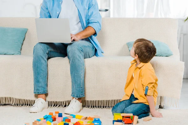 Baba kanepede oturan ve dizüstü renkli yapı taşları ile evde oynarken preschooler oğlu süre kullanma