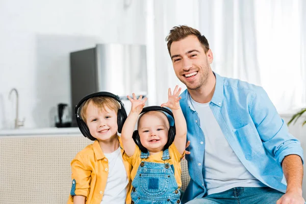 微笑的父亲看着相机与可爱的幼儿和学龄前儿童的儿子在家里的耳机 — 图库照片