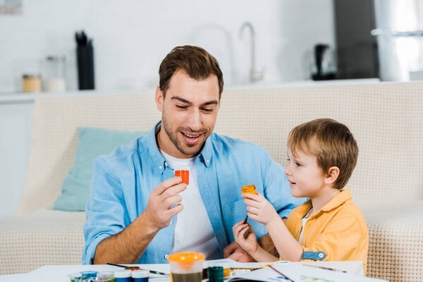 отец и дошкольник сын держит краски во время рисования дома
