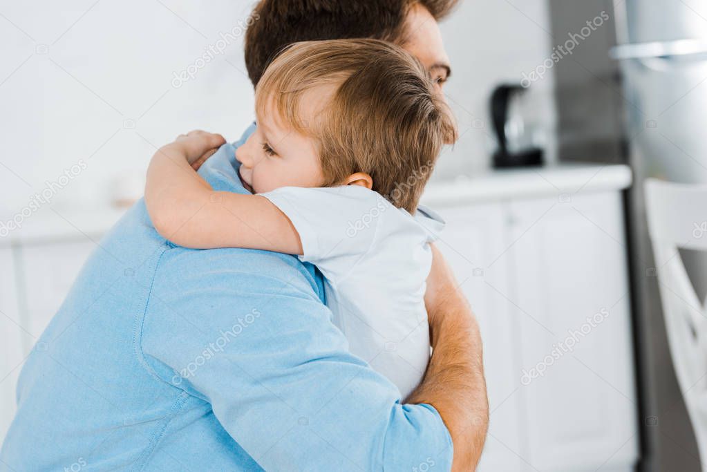 father hugging adorable preschooler son at home with copy space