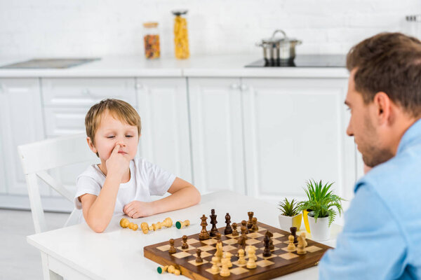 preschooler son picking nose while playing chess with father at home