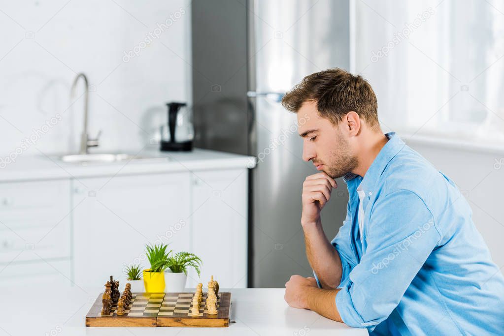 pensive man sitting at table while playing chess at home