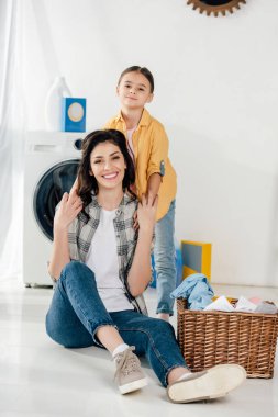 Sarı tişört holding anne çamaşır odasında sepet yakın katta oturan kızı