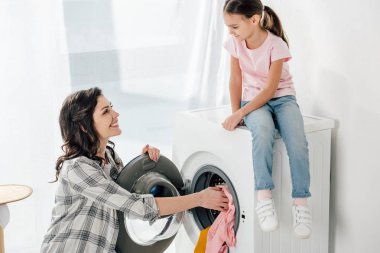 pembe tişört yıkayıcı wile anne gri gömlek giyim çamaşır odasında koyarak oturan kızı
