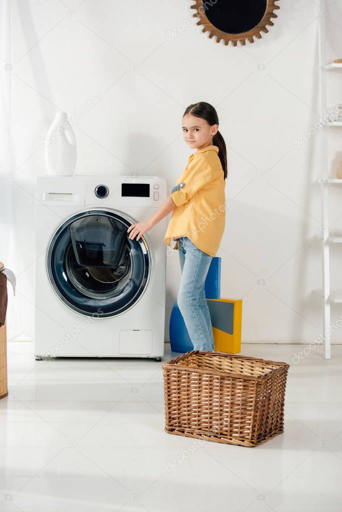 child in yellow shirt near basket opening washer in laundry room