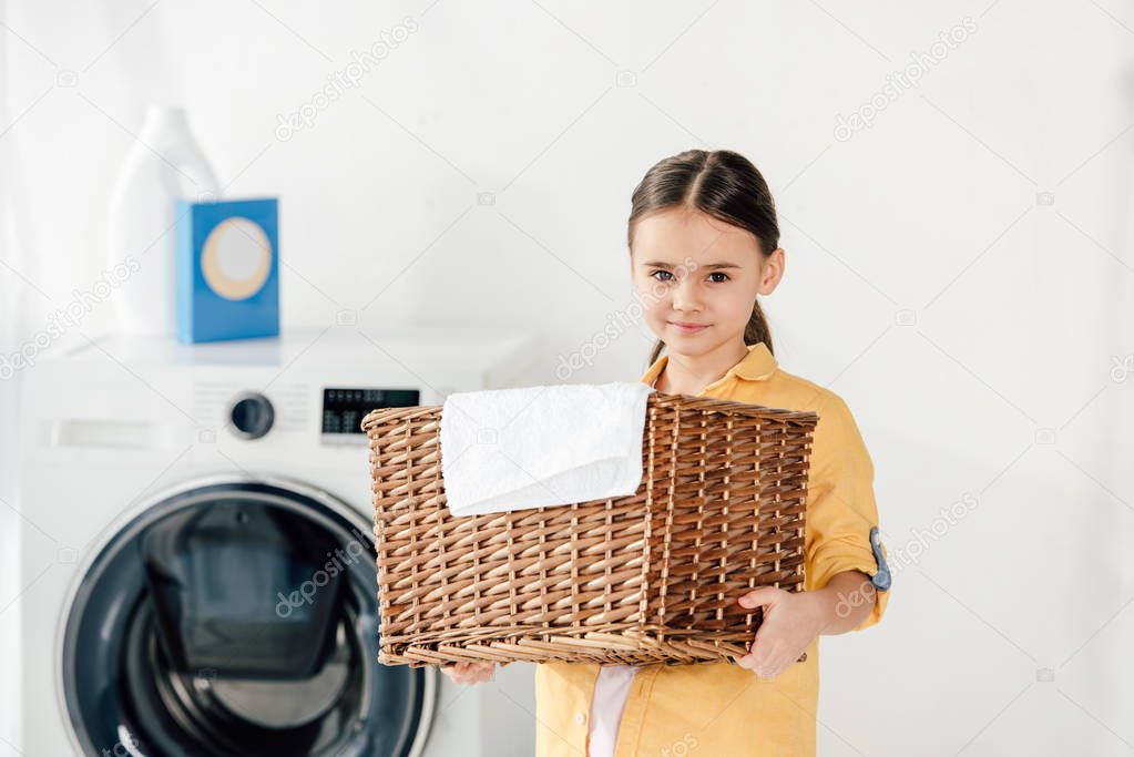 child in yellow shirt holding basket with towel in laundry room